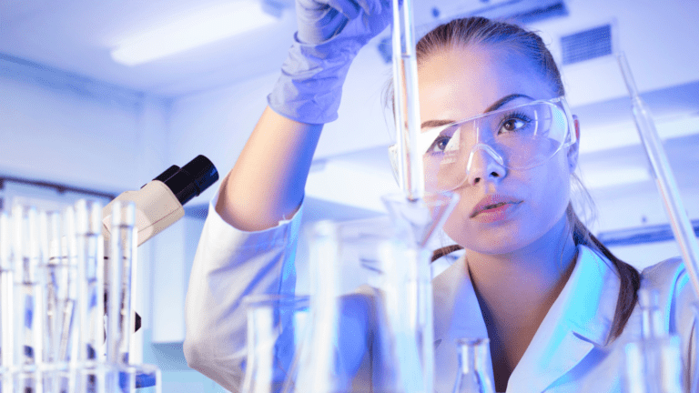 Pesquisadora com óculos de proteção manipulando vidrarias em laboratório, representando duas novas chamadas lançadas pelo MCTI e Finep.