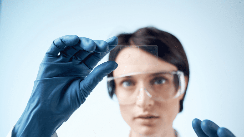Pesquisadora com luvas e óculos de proteção segurando lâmina de microscópio, simbolizando o crescimento de startups de base científica e tecnológica em São Paulo.