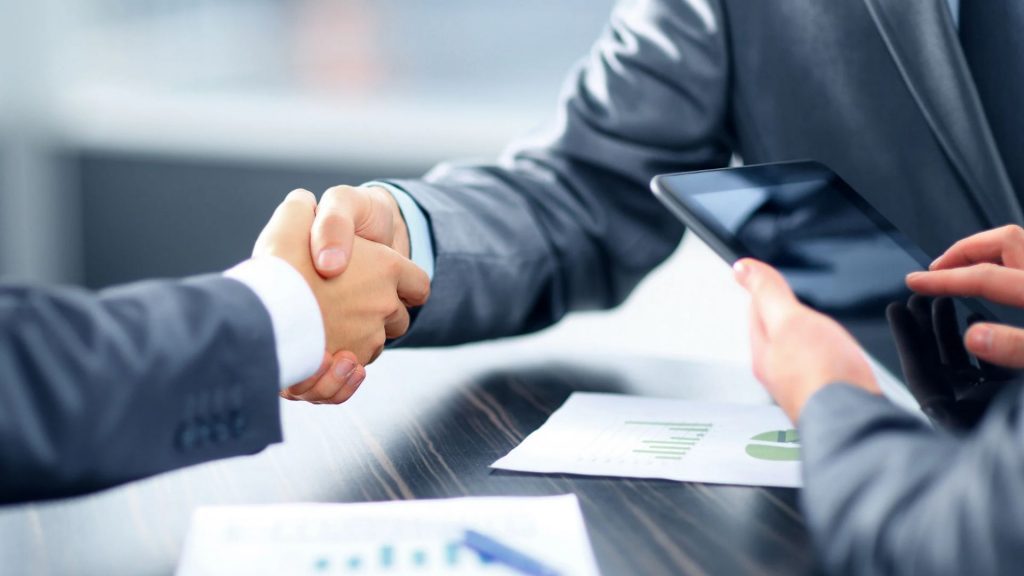 Aperto de mãos entre executivos com tablet e relatório financeiro, representando investimentos e parcerias em inovação na América Latina.