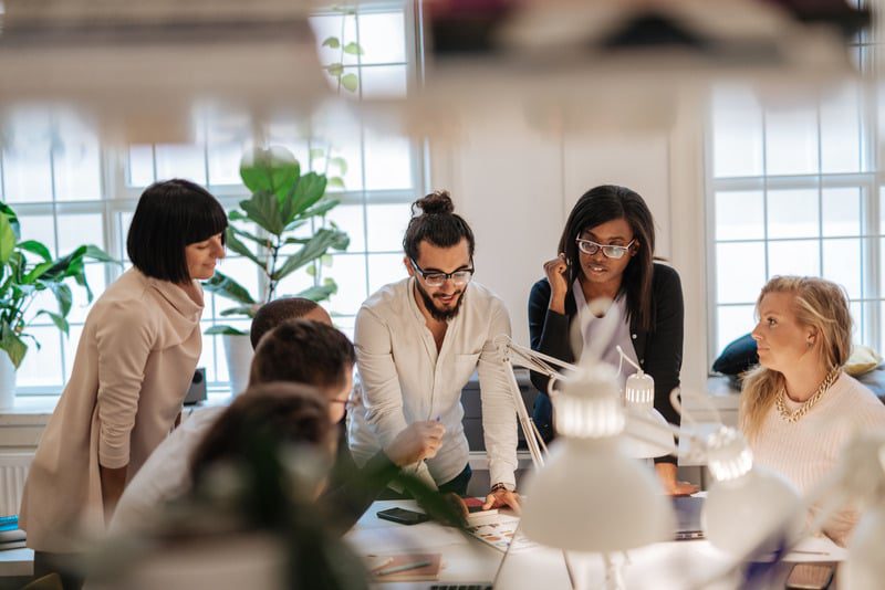Equipe de profissionais em reunião colaborativa ao redor de mesa de trabalho, discutindo estratégias para inovação e alto desempenho com impacto positivo.