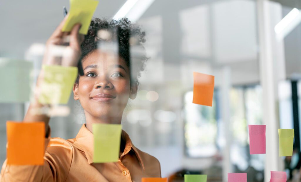 Profissional organiza post-its em parede de vidro — construindo uma cultura de criatividade e experimentação com a gestão da inovação