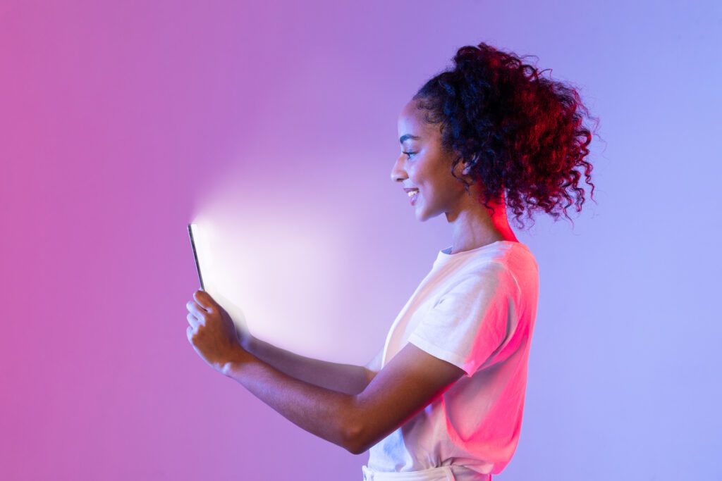 Jovem usando tablet com luz neon roxa e rosa — Governo de São Paulo anuncia o primeiro Distrito de Inovação.