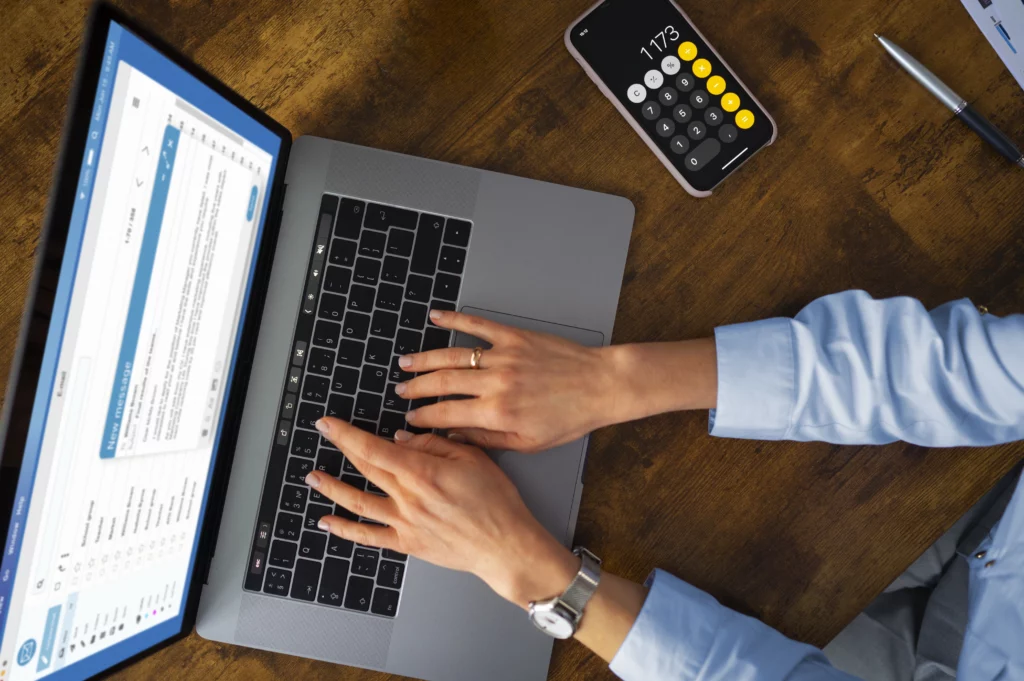 Mãos digitando em notebook com calculadora no celular sobre a mesa — novidades da DIRBI e mudanças para empresas beneficiadas pela Lei do Bem.
