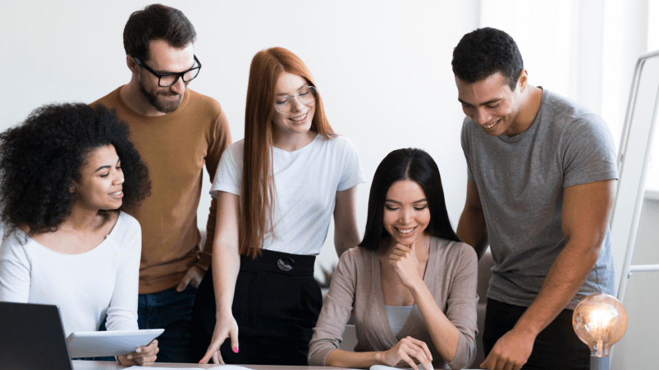 Equipe diversa colaborando ao redor de notebook e lâmpada de ideias — 4 dicas para aumentar a inovação na sua empresa.