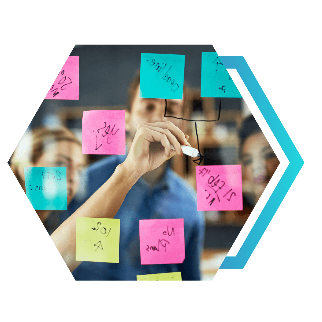 Mão desenhando setas em um vidro, ligando post-its coloridos (rosa e turquesa), com equipe ao fundo — conceito de conectar inovação e estratégia
