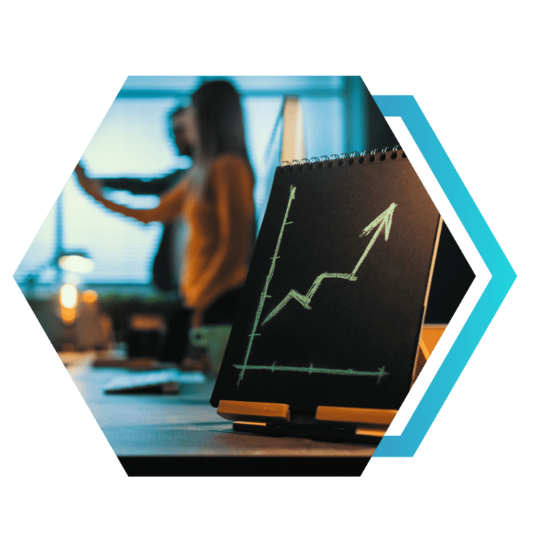 Foto em moldura hexagonal: bloco de notas preto com gráfico de seta ascendente em giz; ao fundo, pessoas desfocadas em escritório