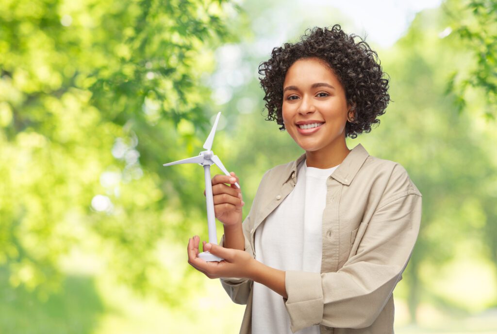 Mulher sorrindo segura um modelo de turbina eólica em área verde, simbolizando energia limpa